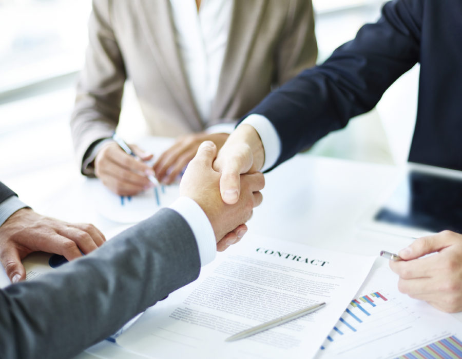 Image of business partners handshaking over business objects on workplace